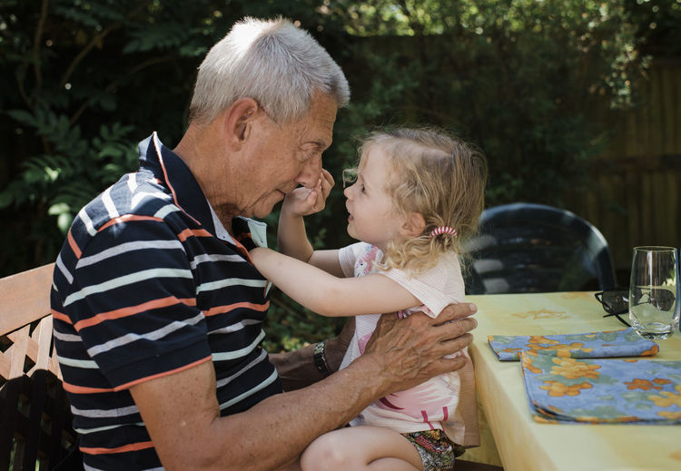 Side view of granddaughter touching grandfather's nose while sitting in yard