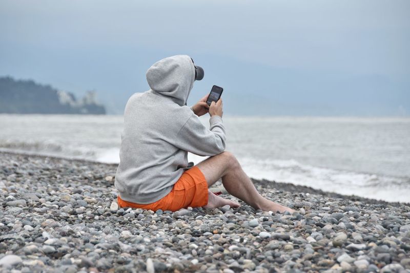 Full length of man photographing sea through mobile phone at beach