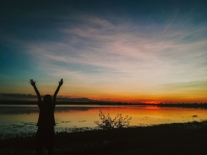 Silhouette person standing by lake against sky during sunset