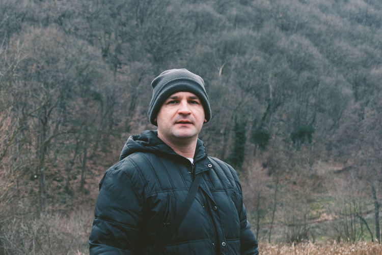 Portrait of man standing against bare trees on mountain