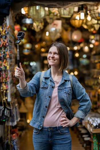 Smiling young woman photographing with camera while standing in store