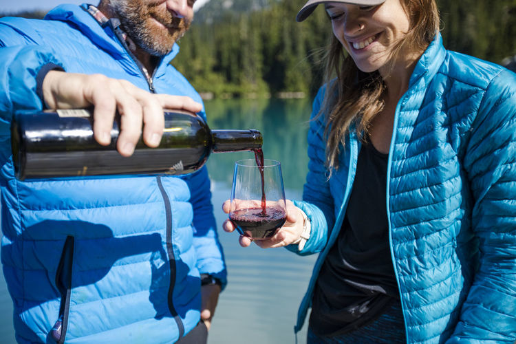 Man pours glass of wine for his partner at the lake.