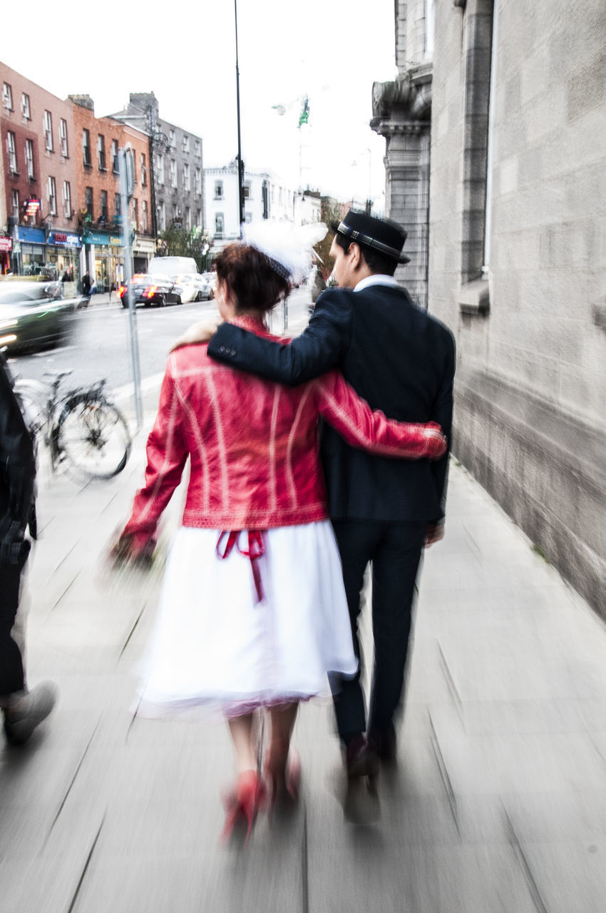REAR VIEW OF COUPLE WALKING ON CITY STREET