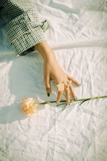 Cropped hand of woman with flower on bed at home