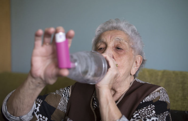 Senior woman using inhaler at home