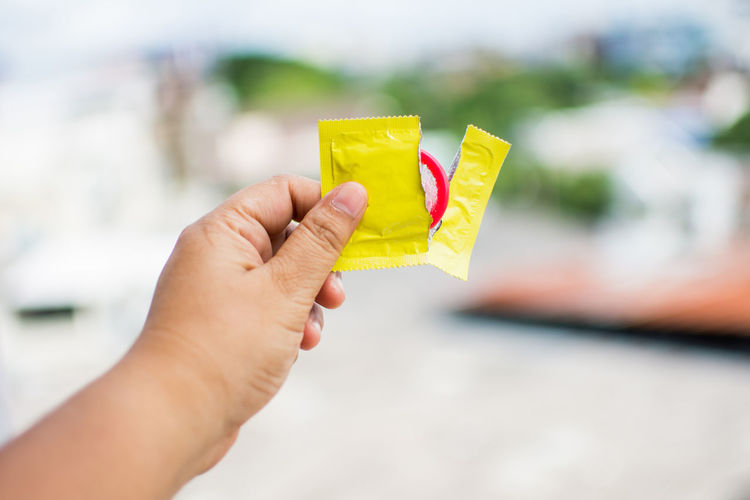 Close-up of man holding condom outdoors