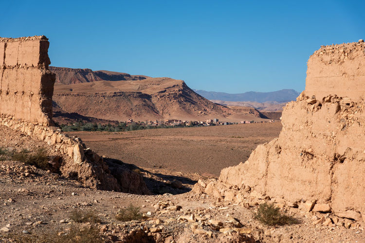 Scenic view of arid plain with village against mountains seen through breach in a mud wall. 