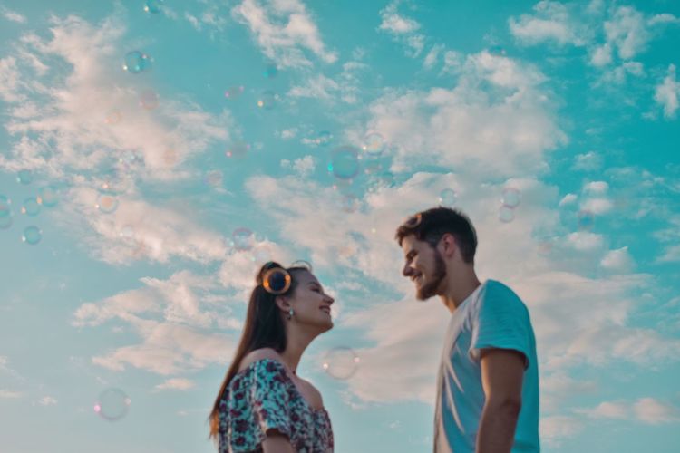 Low angle view of smiling young couple standing against cloudy sky