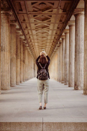 Rear view of young woman photographing with mobile phone while standing in historic building