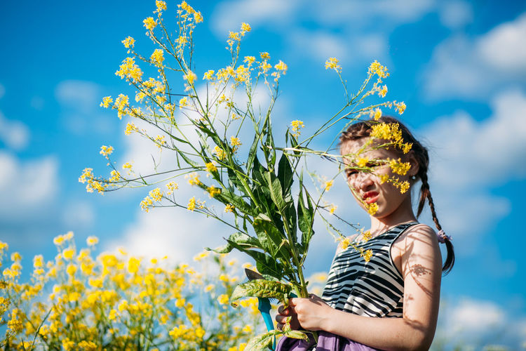 Low section of person standing by yellow flowering plants against sky