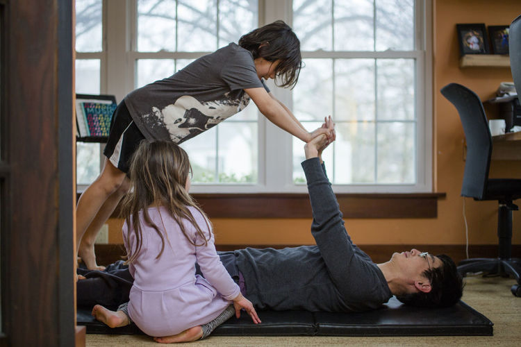 A father does exercise with his two small children inside a home