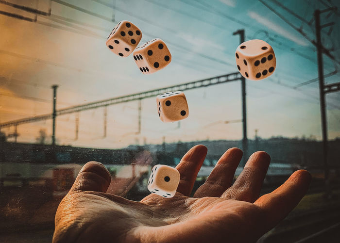 Cropped hand of man throwing dice in air by window