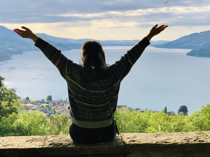 Rear view of woman with arms outstretched standing on landscape at lake thun
