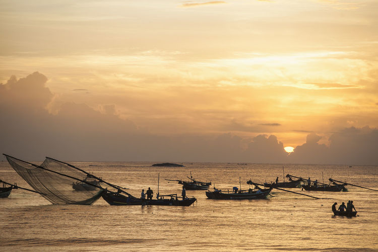 Fishing boats in sea against sky during sunset