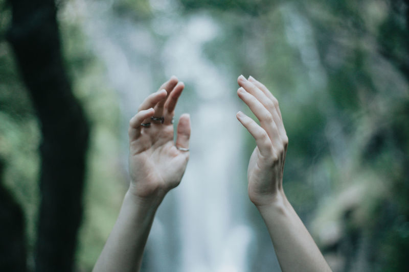 Cropped hand of woman gesturing against trees