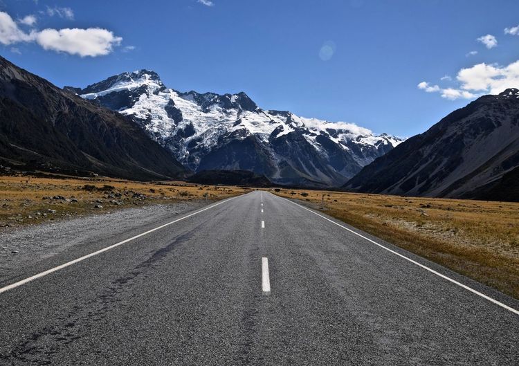 Empty road leading towards snowcapped mountains against blue sky