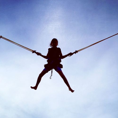 Low angle view of girl bungee jumping against sky