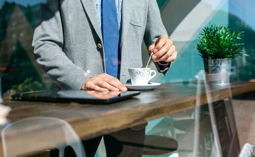 Midsection of businessman with drink standing at table in office