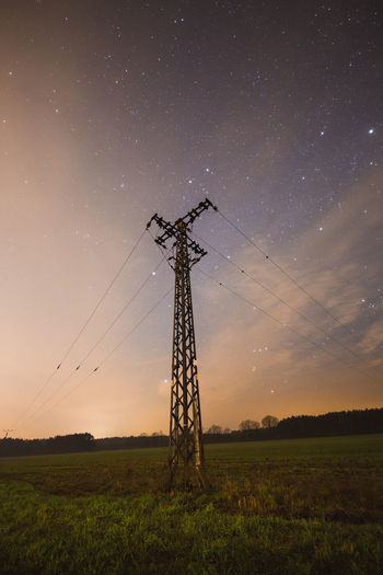 Low angle view of electricity pylon on land against sky at night