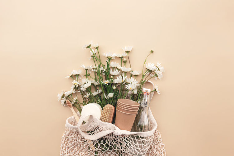 Beige background with eco shopping bag, white chamomile flowers, bath accessories, glass bottle