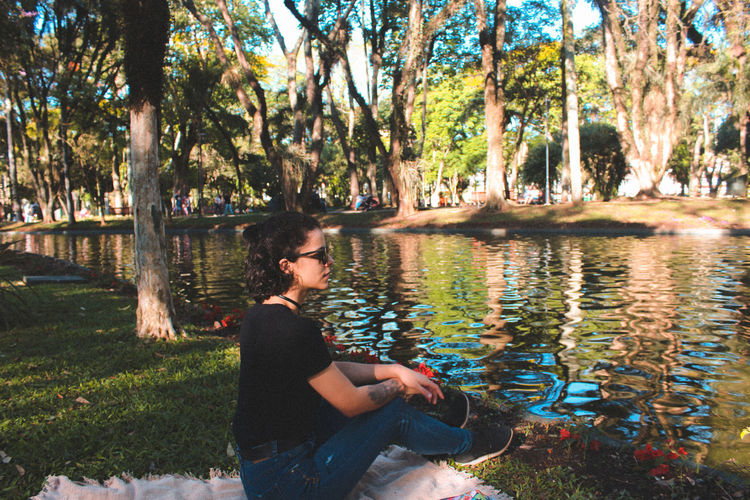 Full length of woman looking away while sitting by lake at park