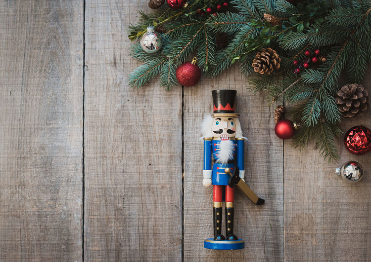 Christmas greenery, nutcracker and decorations against wood backdrop.
