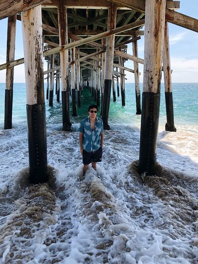 Man standing in sea on shore at beach under pier
