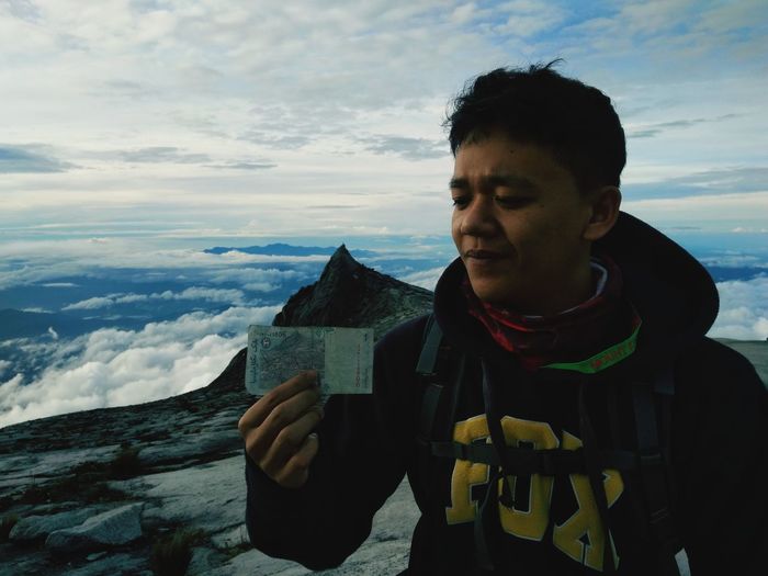 Man looking at paper currency while standing on mountain against sky