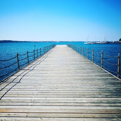 Wooden pier over sea against clear blue sky