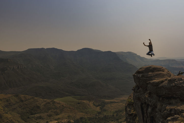 Excited man jumping over rock formation against sky