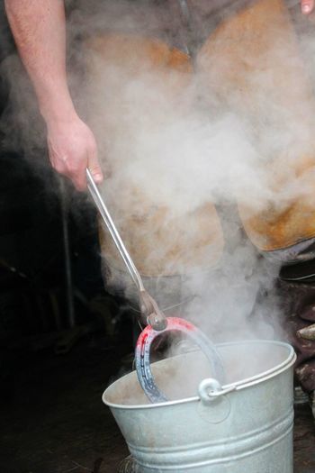 Cropped image of farrier putting hot horseshoe in bucket