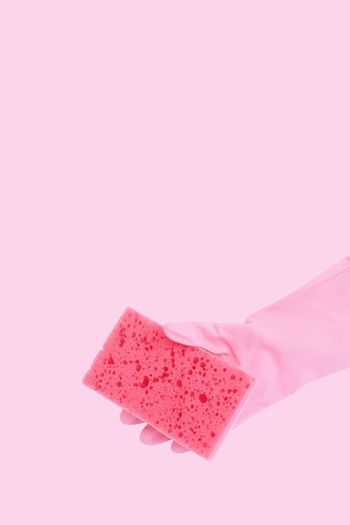 Close-up of hand holding pink sponge against colored background
