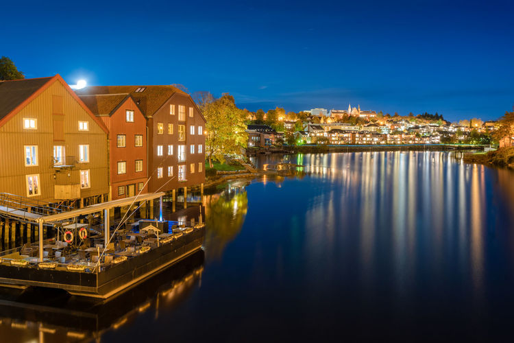 Illuminated buildings by river against sky at night