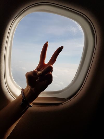 Cropped hand of woman gesturing by airplane window
