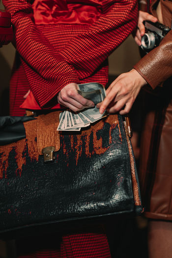 Female body dressed in an  red suit and holding a large leather retro women's bag and paper dollars