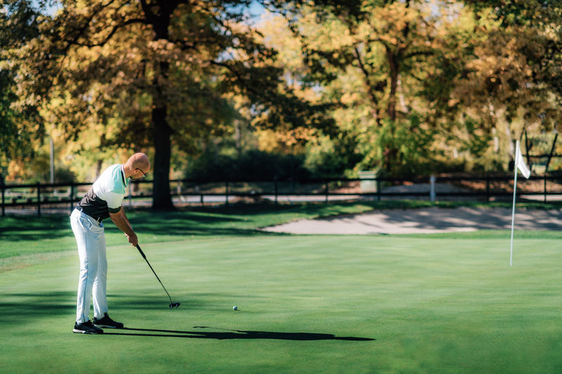 Young golfer putting on the green in a sunny autumn day
