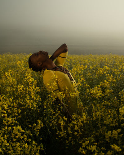 Young man standing amidst yellow flowers on oilseed rape landscape