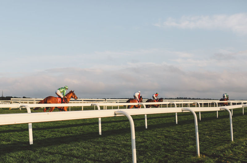 Jockey riding horses at epsom downs racecourse against sky