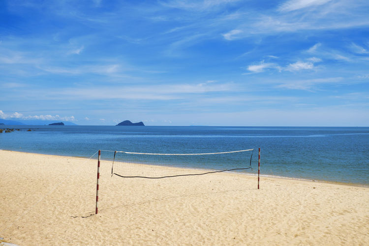Scenic view of deserted beach with volleyball net against sunny sky