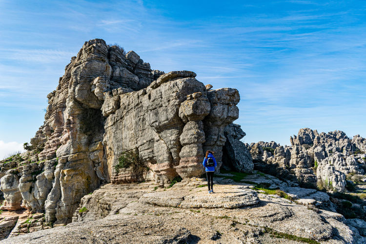 Rear view of woman standing on rock by mountain against sky