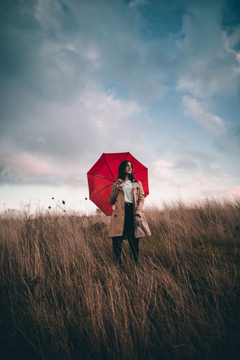 Young girl with a trench and a red umbrella in a field
