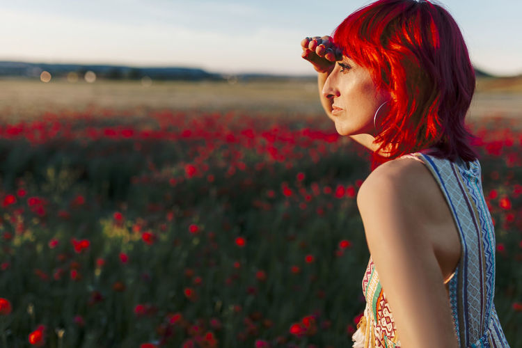 Redheaded woman shielding eyes while looking away during sunset