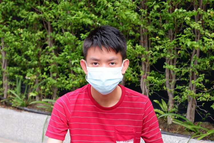 Red t-shirt boy with mask in green background.