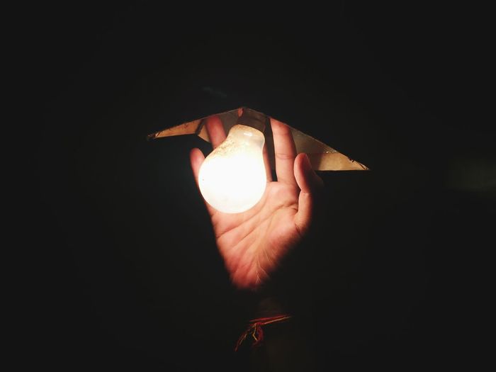 Cropped image of hand by illuminated light bulb