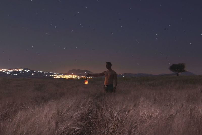 Shirtless man with illuminated lantern standing on field