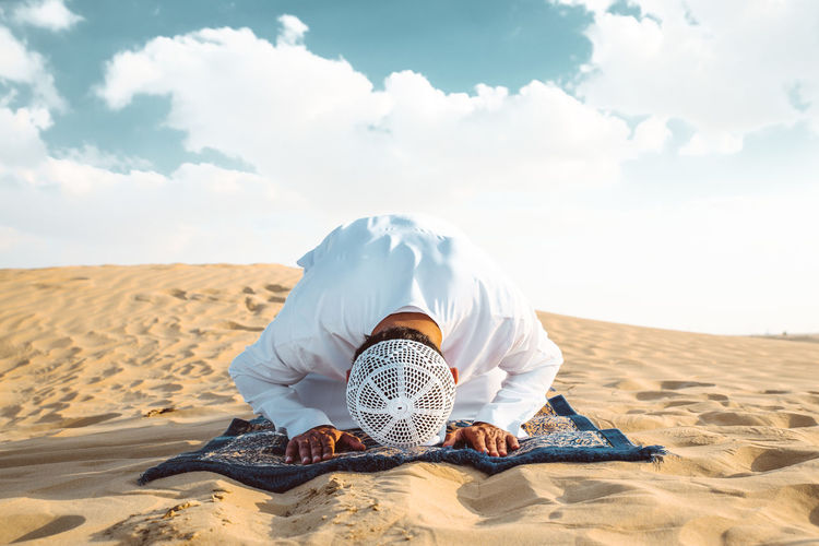 Man sitting on sand dune in desert against sky