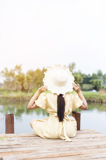 Rear view of woman sitting on wood against lake
