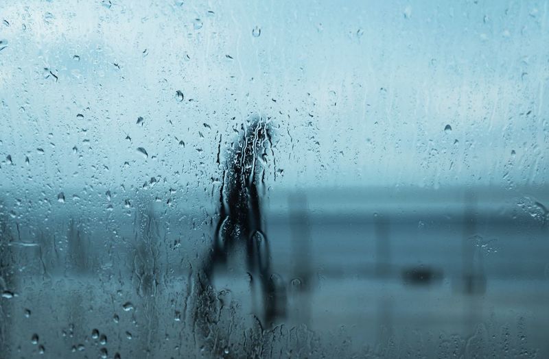 Person seen through of wet glass window in rainy season
