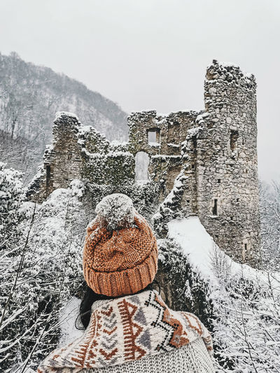 Rear view of young woman in winter clothes looking at castle ruins in winter, snow.