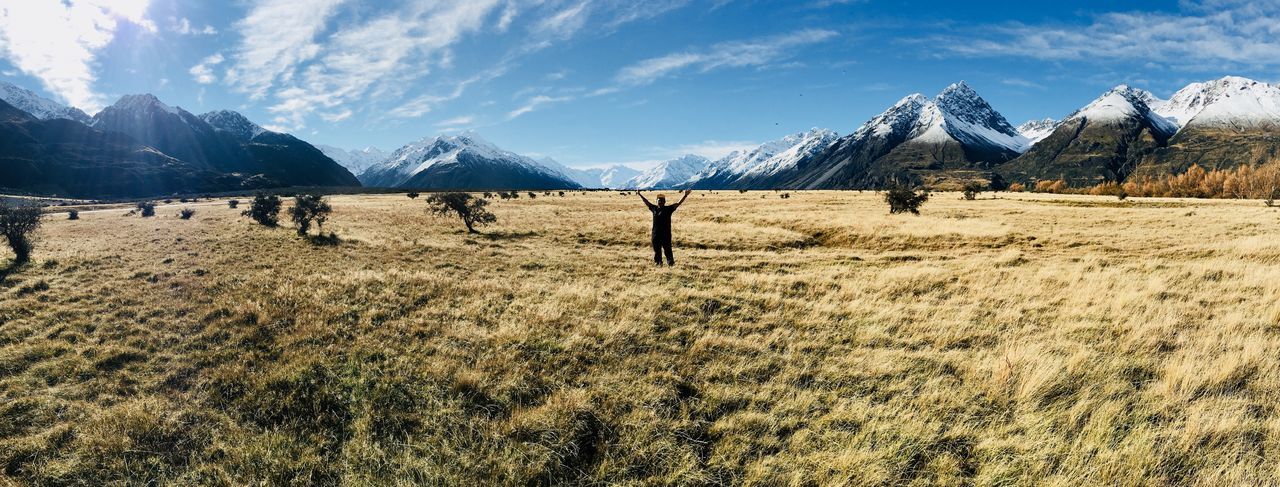 Man with arms raised on field against snowcapped mountains 